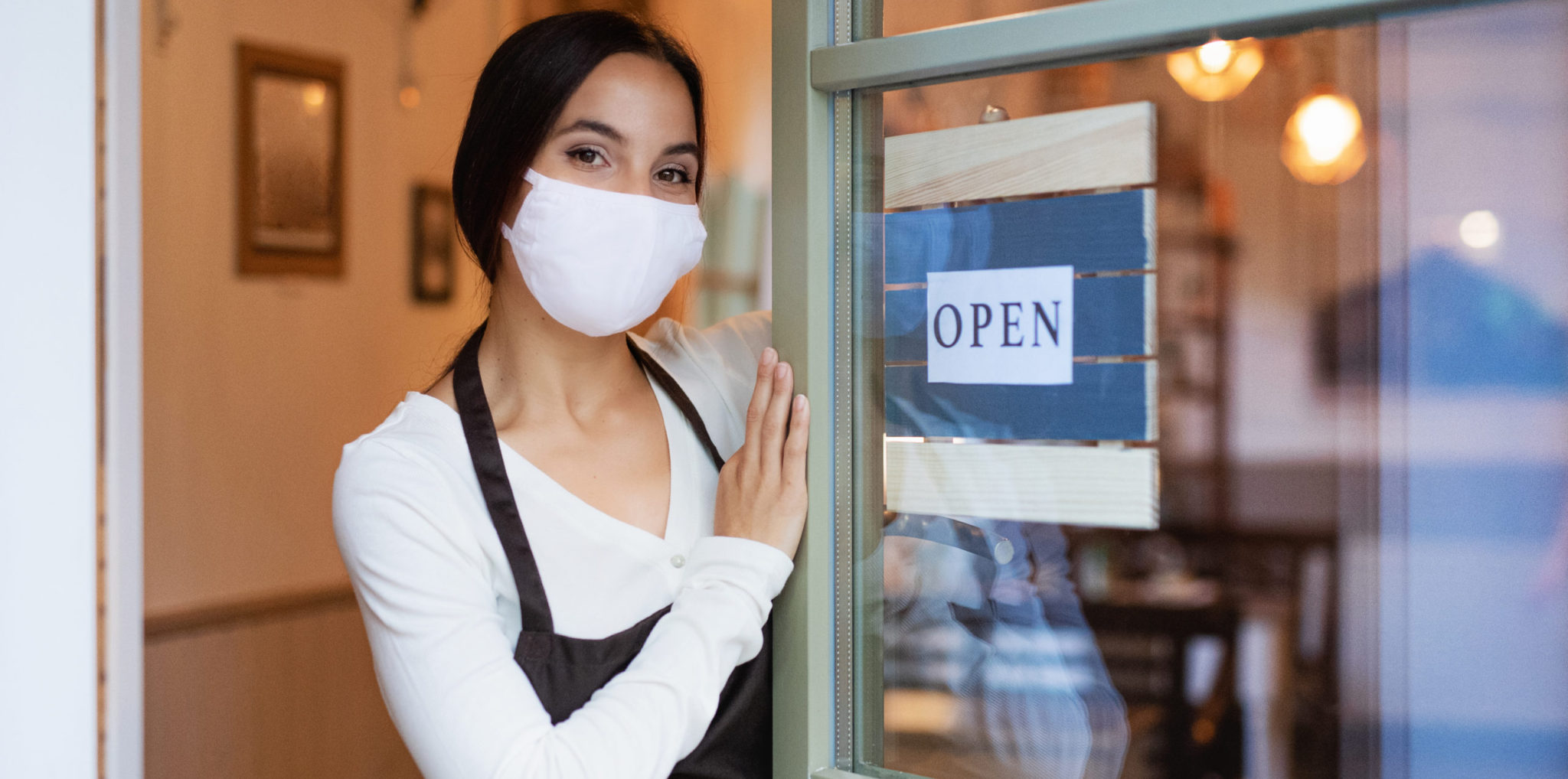 Young Waitress With Face Mask By Entrance Door In Cafe Reopening